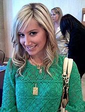 Юная блондинка улыбается, на ней надета зеленая блузка и три золотых цепи на шее, на одной из которых висит золотая медаль